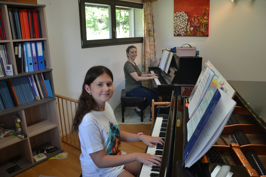 Linda Gysin, de Valangin (Neuchâtel), au piano à l'arrière-plan, et une jeune fille au piano au premier plan.